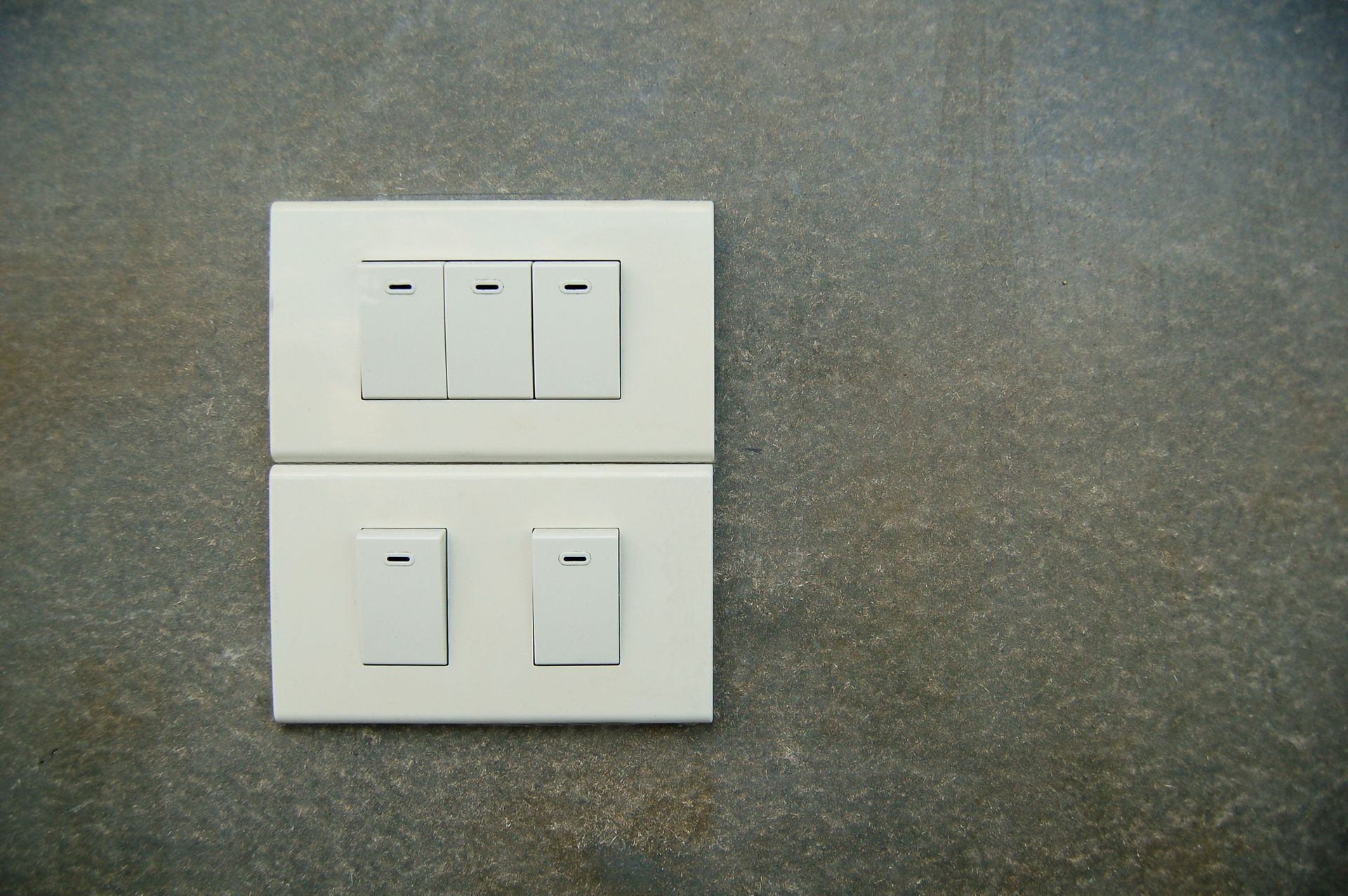 Minimalist photo of white electrical rocker switches on a textured stone wall background.